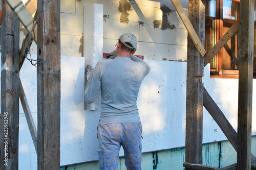 Worker installing white rigid polyurethane foam sheet on aerated concrete block wall for energy saving. Diy, house improvement and insulation concept.