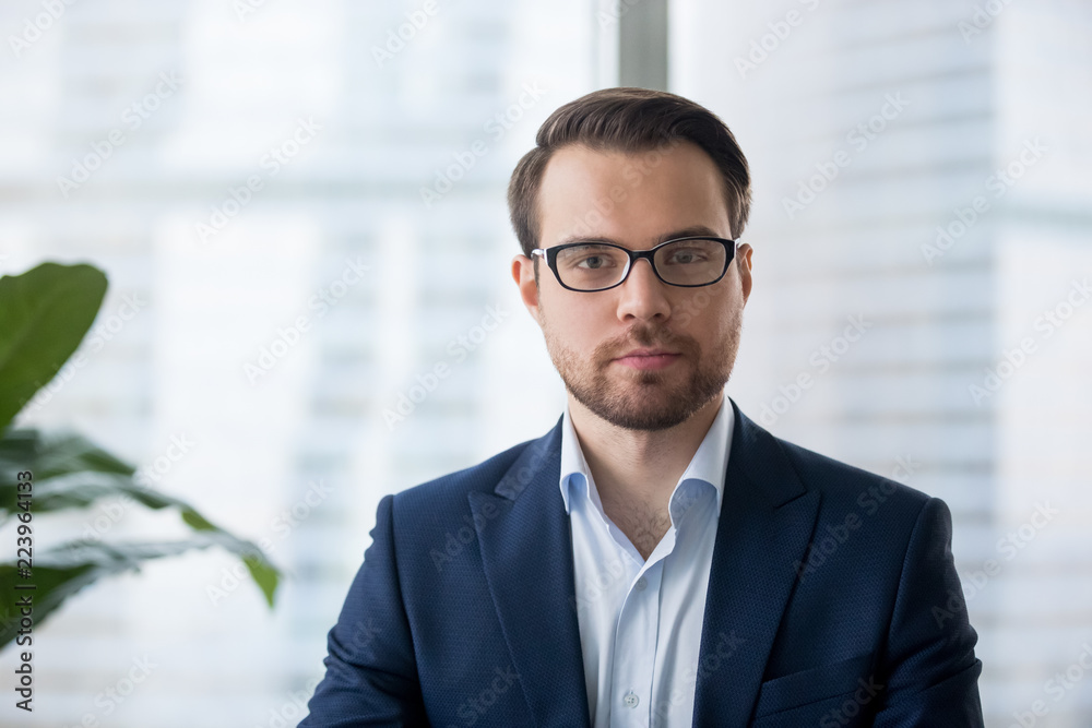 Portrait of serious millennial businessman wearing glasses looking at  camera, headshot of concentrated confident male worker or director posing  in modern office, making photo or picture near window Stock Photo | Adobe