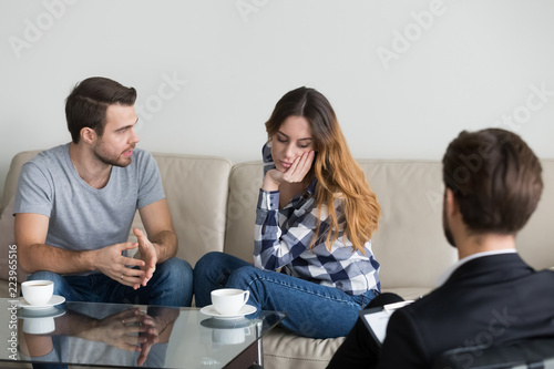 Millennial couple discuss family problems sitting on couch at counselor or psychologist, male relationship expert help husband and wife, saving marriage or overcoming difficulties at therapy session