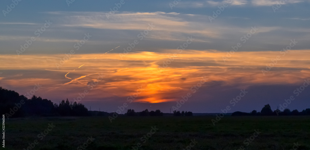 Beautiful sunset in the field. Red, yellow, blue sky. Summer evening.