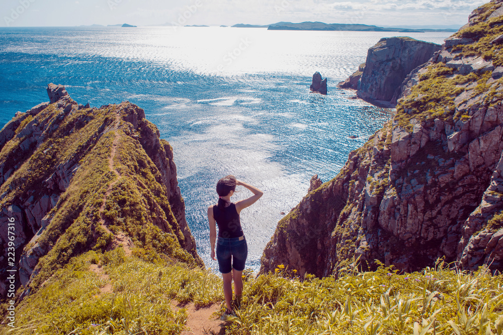 Lonely girl standing on a rocky shore and looking into the distance. Girl on background of beautiful wildlife, sea and rocks