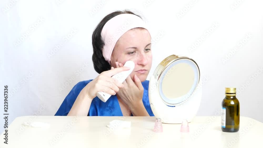 Young woman with a device performs microdermabrasion of the skin of the face on a white background. The concept of beauty and skin care. Young woman with a device performs microdermabrasion of the skin of the face on a white background. The concept of beauty and skin care.