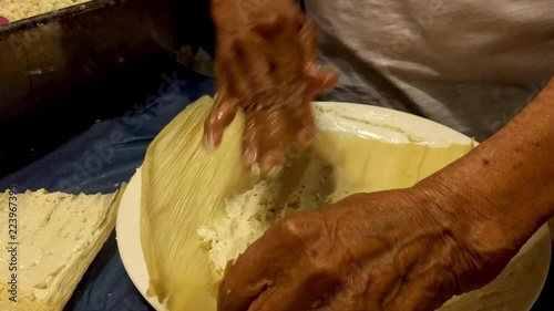 An elderly Mexican woman is spreading masa on a corn husk to make homemade tamales. Traditional Mexican food.