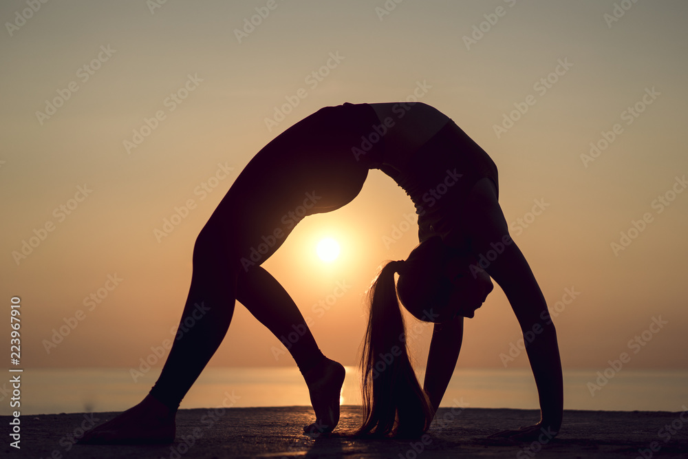 Silhouette of young woman practicing yoga, wheel pose or Urdhva  Dhanurasana. Healthy girl doing stretching on the beach on the sunrise.  Relaxing early in the morning. Stock Photo | Adobe Stock