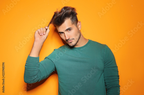 Young man with comb posing on color background. Trendy hairstyle
