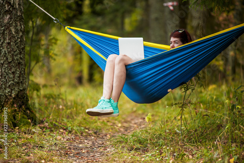 Image of brunette resting in hammock with laptop in forest © Sergey