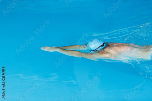 Portrait of sports man in blue cap swimming under water in pool
