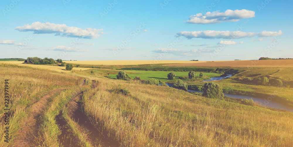 Beautiful view of country ground road,river curve,green and yellow fields illuminated by the warm light of setting sun.Summer sunny country landscape.Tula region,Russia.