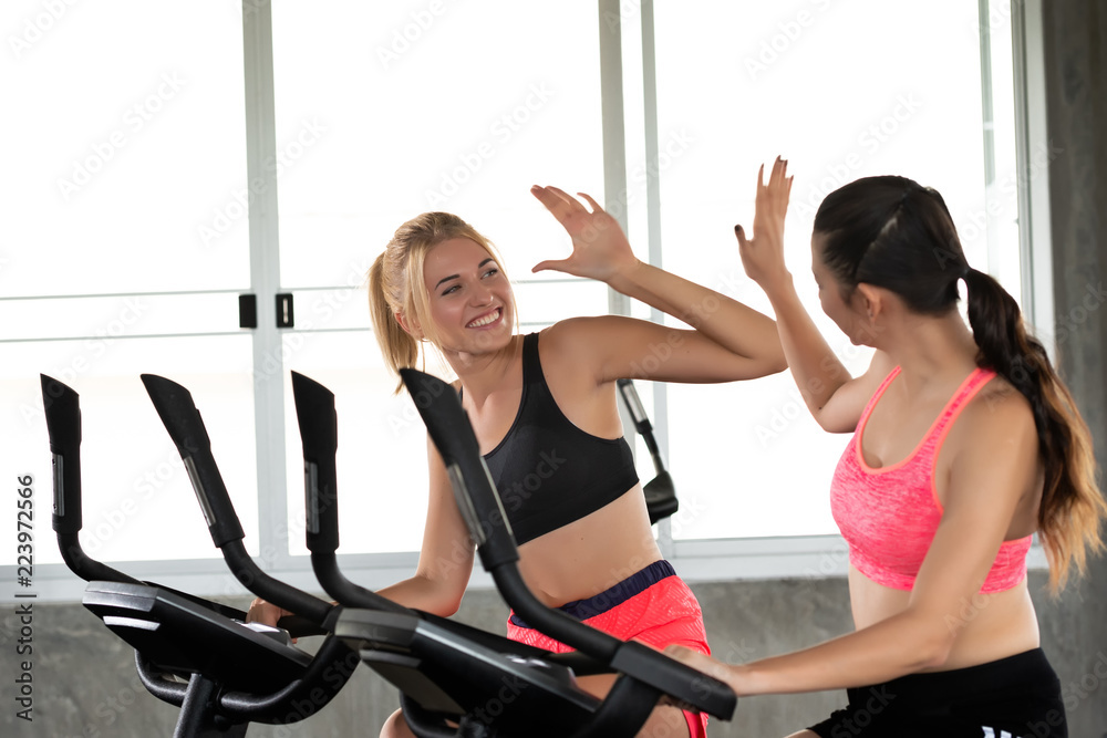 We did it Two young girls are smile happy and giving high five with exercise bike at the gym. fitness and healthy lifestyle concept. Stock Photo Adobe Stock