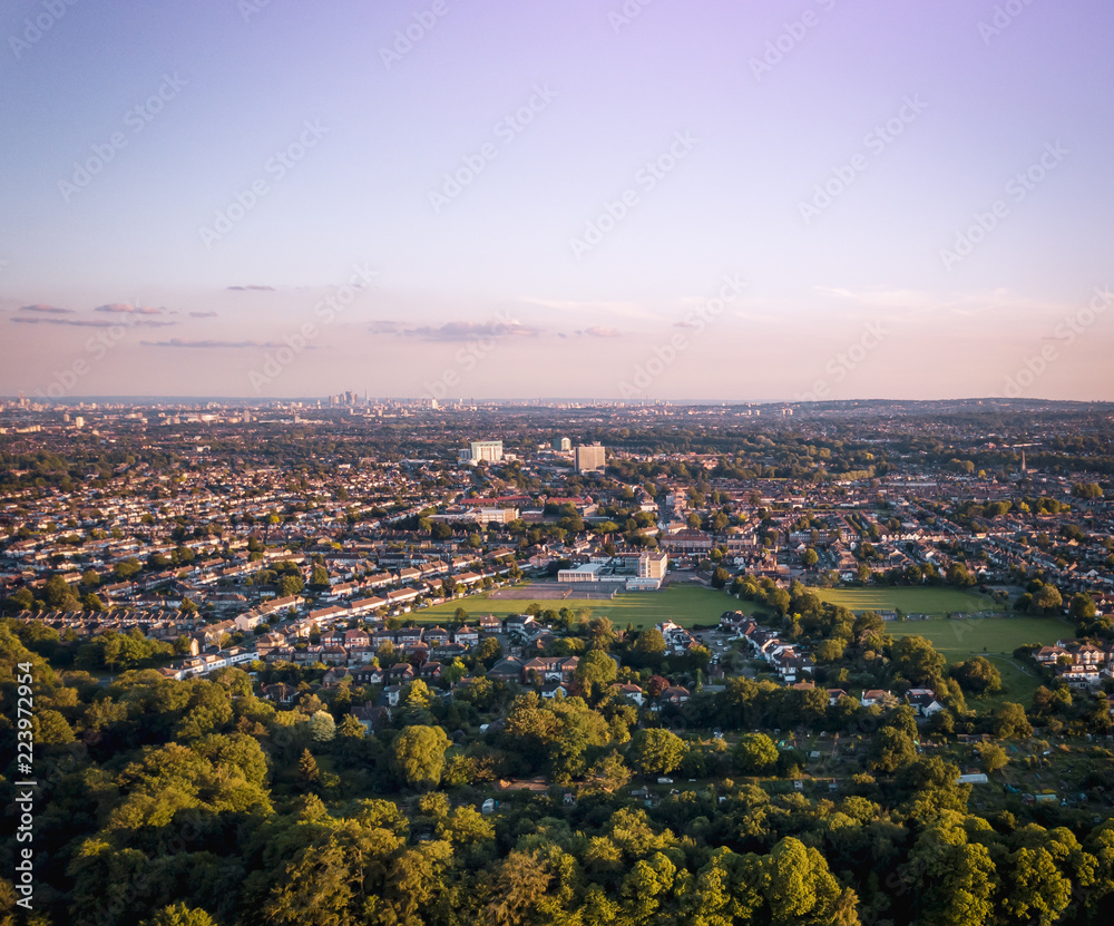 Sunrise aerial view of houses in London above a London housing estate next to countryside and farm land. Fields and community housing can be seen in the foreground