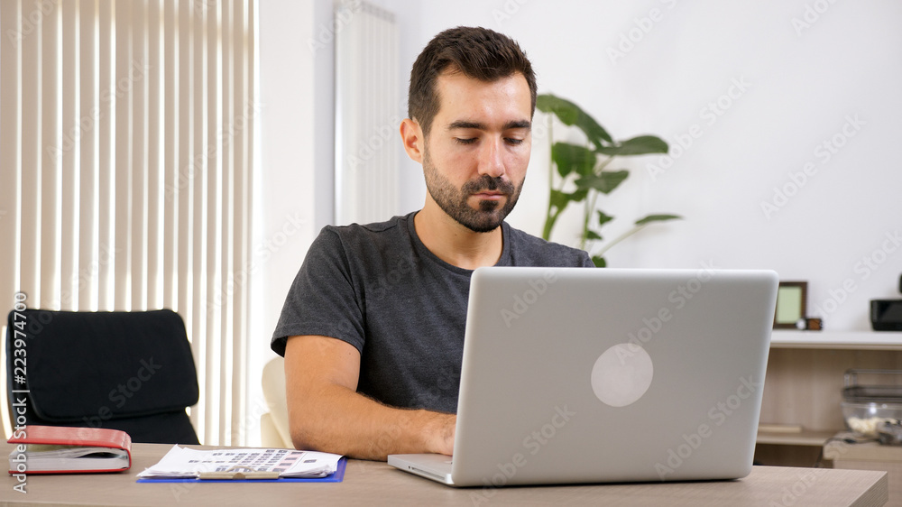 Young man working with laptop at his business documentation . Business person at workplace. Young man working with laptop at his business documentation . Business person at workplace.
