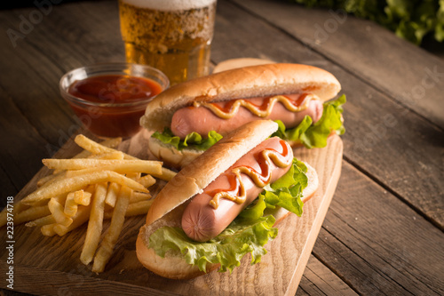 Photo of barbecue grilled hot dog with yellow mustard and ketchup on wooden background. Hot dog sandwich with potato fries and sauces.