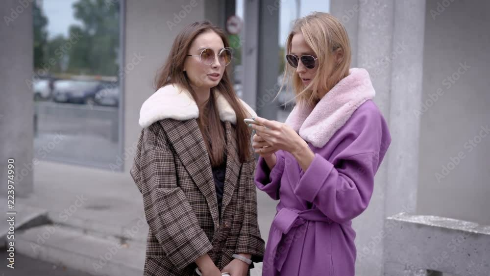 Two women standing outside in autumn looking stylish, two friends talking. Two women standing outside in autumn looking stylish, two friends talking.