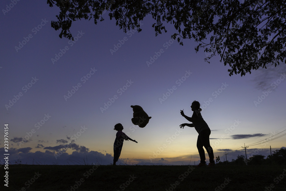 A small girl playing with bear and her mother in the park at sunset. A small girl playing with bear and her mother in the park at sunset.