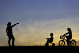 The silhouette photo of mother and her daughter riding bicycle in the park with sweet sky at sunset.