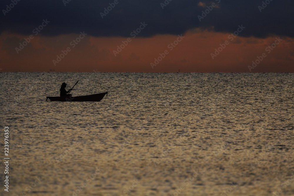 The silhouette of a woman paddle boat in the sea at twilight.