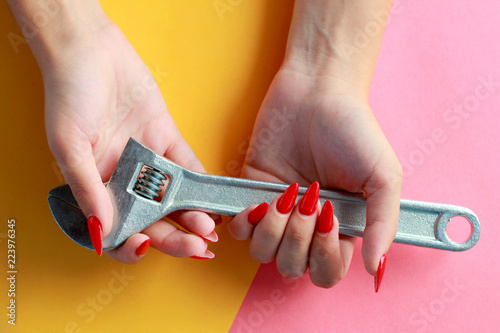 Fun minimal concept. Woman hands with Adjustable wrench, spanner. Top view. Pastel colours background. Trendy colors.