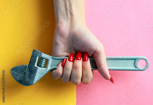 Fun minimal concept. Woman hands with Adjustable wrench, spanner. Top view. Pastel colours background. Trendy colors.