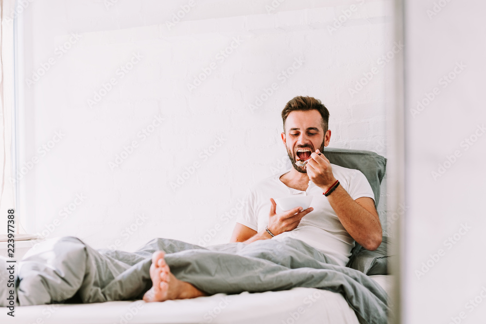 Young man eating breakfast in bed