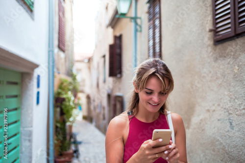 Cheerful tourist woman using smart phone on old narrow street in Croatia, travel lifestyle