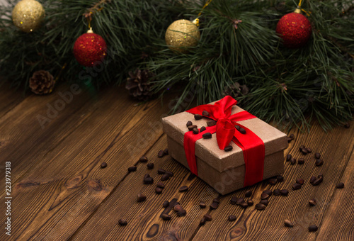 A box with a Christmas gift tied with a red ribbon and sprinkled with pine nuts on a wooden background  in the background a Christmas tree with Christmas toys  a gift for Christmas and a new year