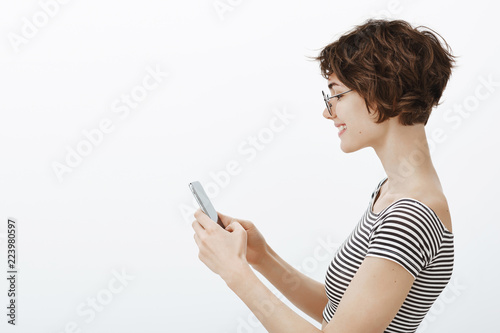 Just a sec I need answer this message. Portrait of good-looking tender young woman with stylish short haircut and glasses, holding smatphone and typing feedback about great cafe she visited