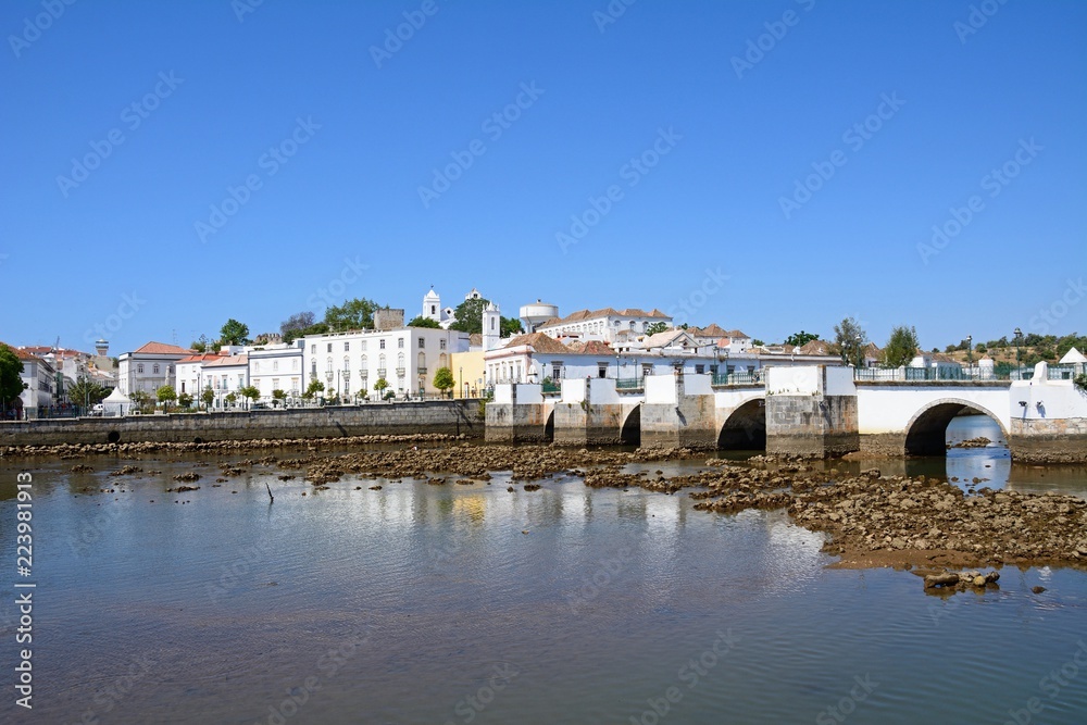 View of the Roman bridge (Ponte Romano) and Gilao river with town buildings to the rear, Tavira, Portugal. View of the Roman bridge (Ponte Romano) and Gilao river with town buildings to the rear, Tavira, Portugal.