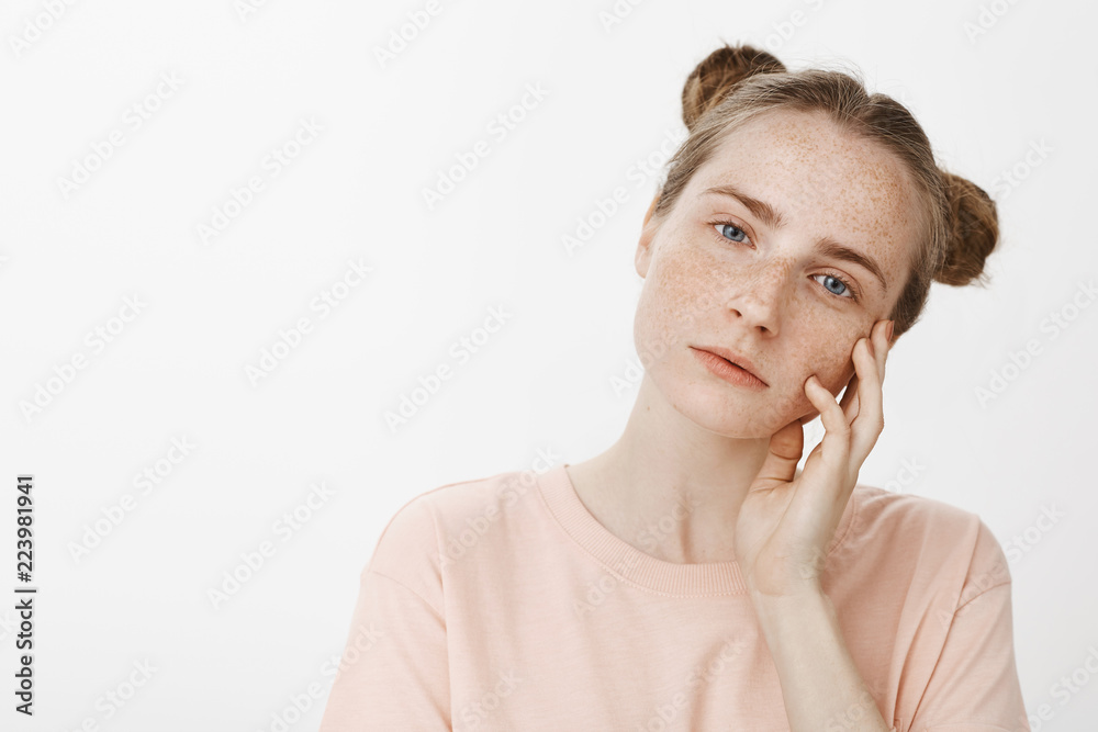 Dreamy good-looking feminine female model with cute blue eyes and freckles, tilting head and touching face gently with palm, gazing at camera with tender expression, standing over gray wall Dreamy good-looking feminine female model with cute blue eyes and freckles, tilting head and touching face gently with palm, gazing at camera with tender expression, standing over gray wall