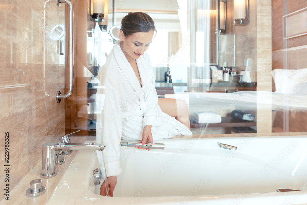 Woman in luxurious hotel bathroom letting water in the bathtub in animation of a relaxing experience Woman in luxurious hotel bathroom letting water in the bathtub in animation of a relaxing experience