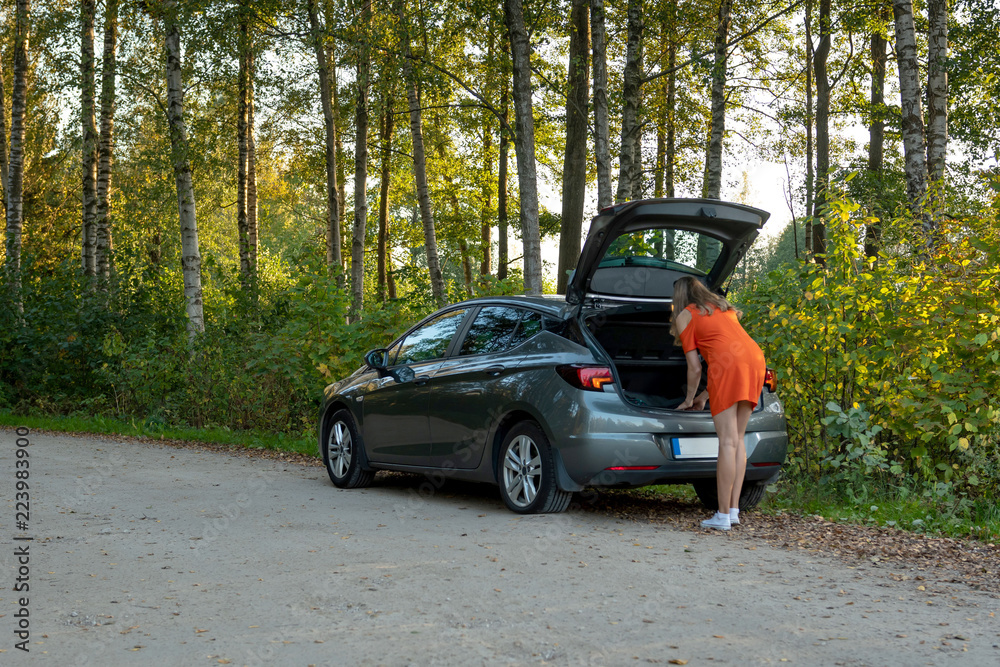 A beautiful young woman looking for a spare wheel in a car boot