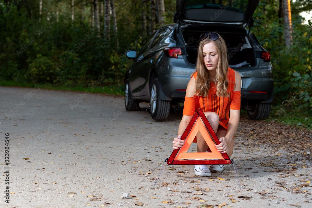 girl sets a triangle in back of broken car