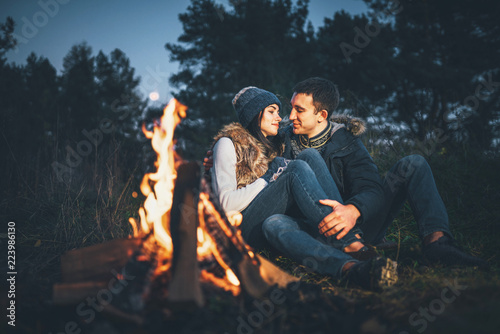 Pretty couple relaxing near bonfire in the forest at evening time