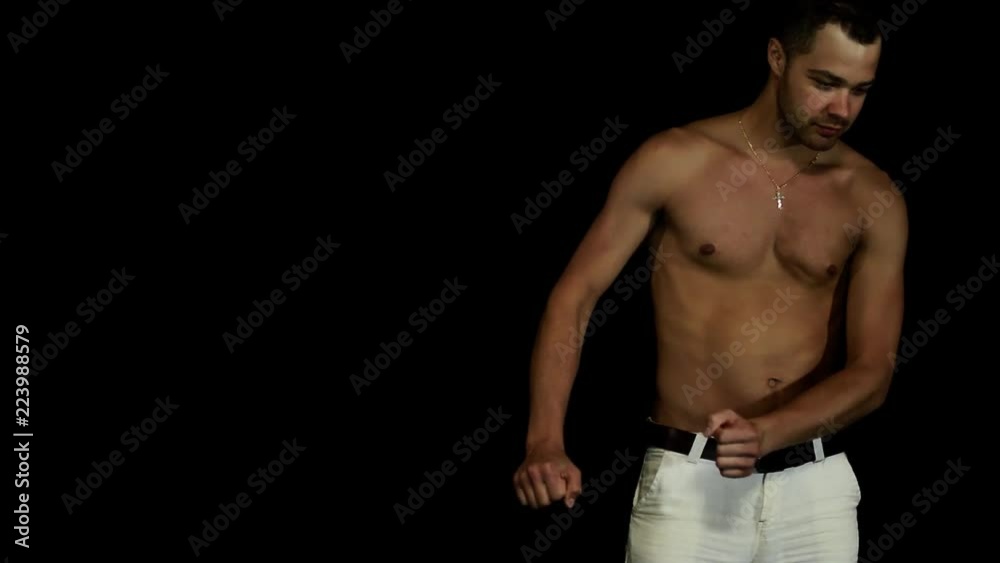 Mature sporty handsome tanned brown eyed male with naked torso and wearing white pants with black leather belt starts slowly, with hesitation dancing in front of camera on black matte background. Mature sporty handsome tanned brown eyed male with naked torso and wearing white pants with black leather belt starts slowly, with hesitation dancing in front of camera on black matte background.