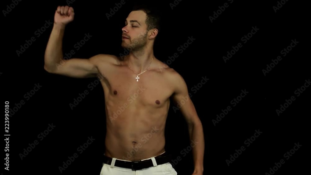 Bearded sporty sexy tanned brown eyed, young man with naked torso and wearing white pants with black leather belt is energetically dancing in front of camera on black matte background Bearded sporty sexy tanned brown eyed, young man with naked torso and wearing white pants with black leather belt is energetically dancing in front of camera on black matte background