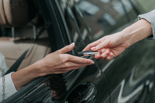 Close up female arm giving key from modern car for girl. She locating in vehicle while putting arm through window