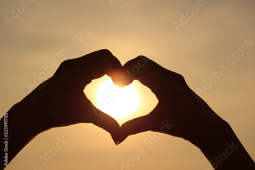 Silhouette of female s hand posing LOVE HEART sign against the shiny rising sun 
