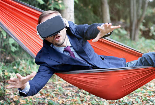 Surprised businessman uses vr glasses, resting in a hammock. Virtual reality or future technology concept