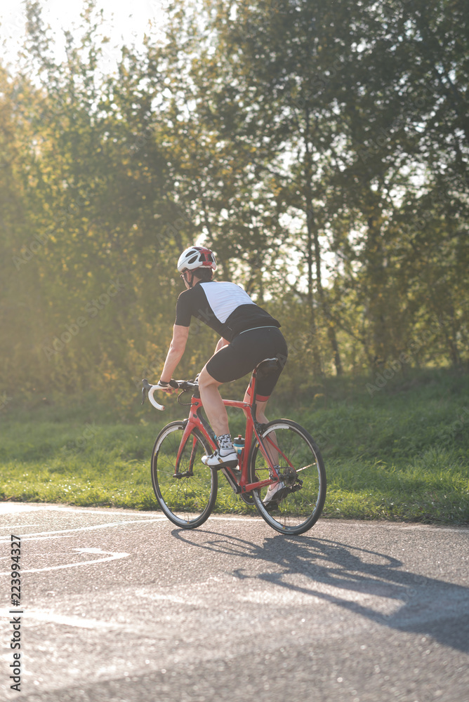 Active male athlete riding bicycles on an open asphalt road. Hills with green grass and the sunset