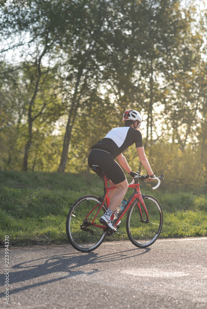 Active male athlete riding bicycles on an open asphalt road. Hills with green grass and the sunset