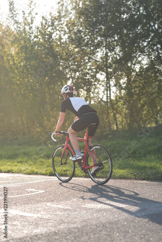 Fototapeta Naklejka Na Ścianę i Meble -  Active male athlete riding bicycles on an open asphalt road. Hills with green grass and the sunset