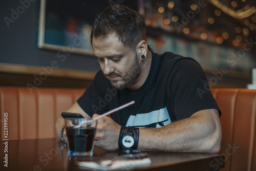 Young attractive man looking at mobile phone screen and drinking soda.