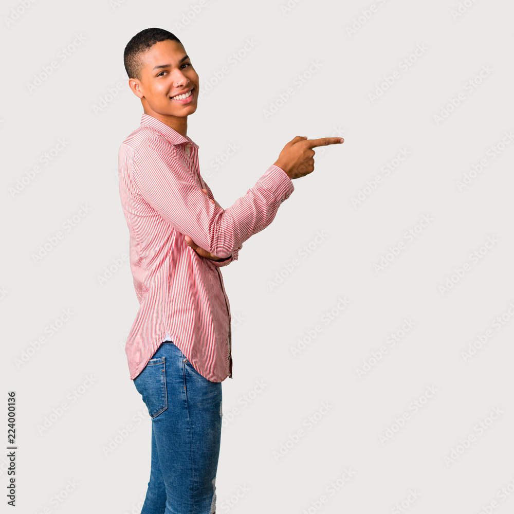 Young african american man pointing finger to the side and presenting a product in lateral position on grey background Young african american man pointing finger to the side and presenting a product in lateral position on grey background