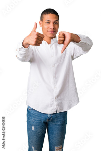Young african american man with white shirt making good-bad sign. Undecided person between yes or not on isolated white background