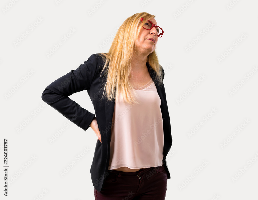 Middle-age blonde business woman with black jacket unhappy and suffering from backache for having made an effort on isolated grey background Middle-age blonde business woman with black jacket unhappy and suffering from backache for having made an effort on isolated grey background