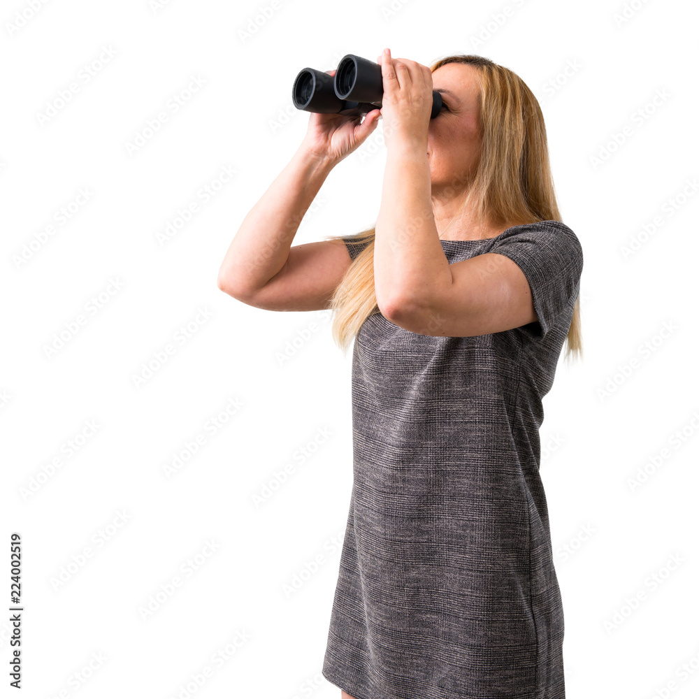Middle-age blonde woman and looking for something in the distance with binoculars on isolated white background