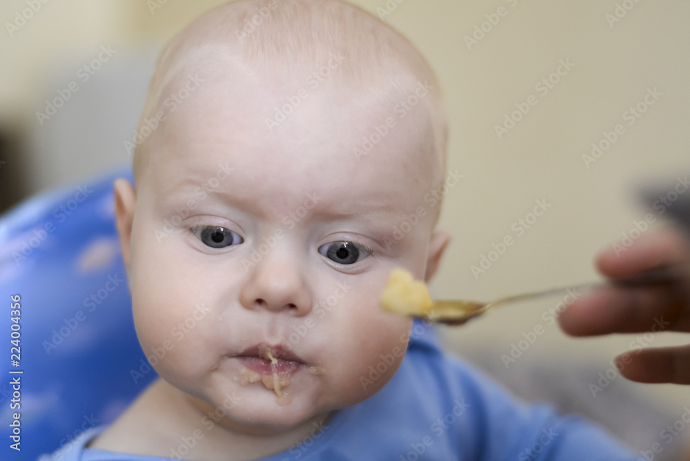 Mom feeds her son from a spoon with applesauce Mom feeds her son from a spoon with applesauce