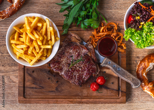 Fototapeta Naklejka Na Ścianę i Meble -  Rinder Steak auf dem Oktoberfest mit Pommes Frites Röst Zwiebeln und Salt auf einem Holz Brett mit einem Jagd Messer