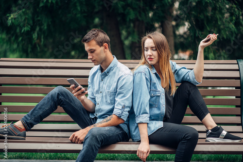 Phone addiction, young couple on the bench in park