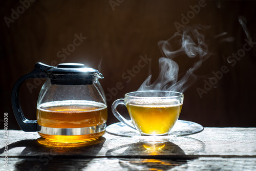 Hot tea in glass teapot and cup with steam on wood background