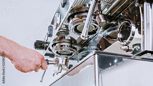 Hands of professional barista standing near the big metal coffee machine and looking how coffee pouring into the white cups